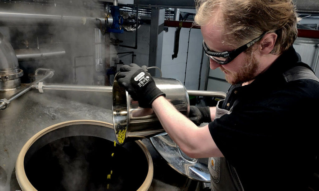 Brewer pouring hops into vat